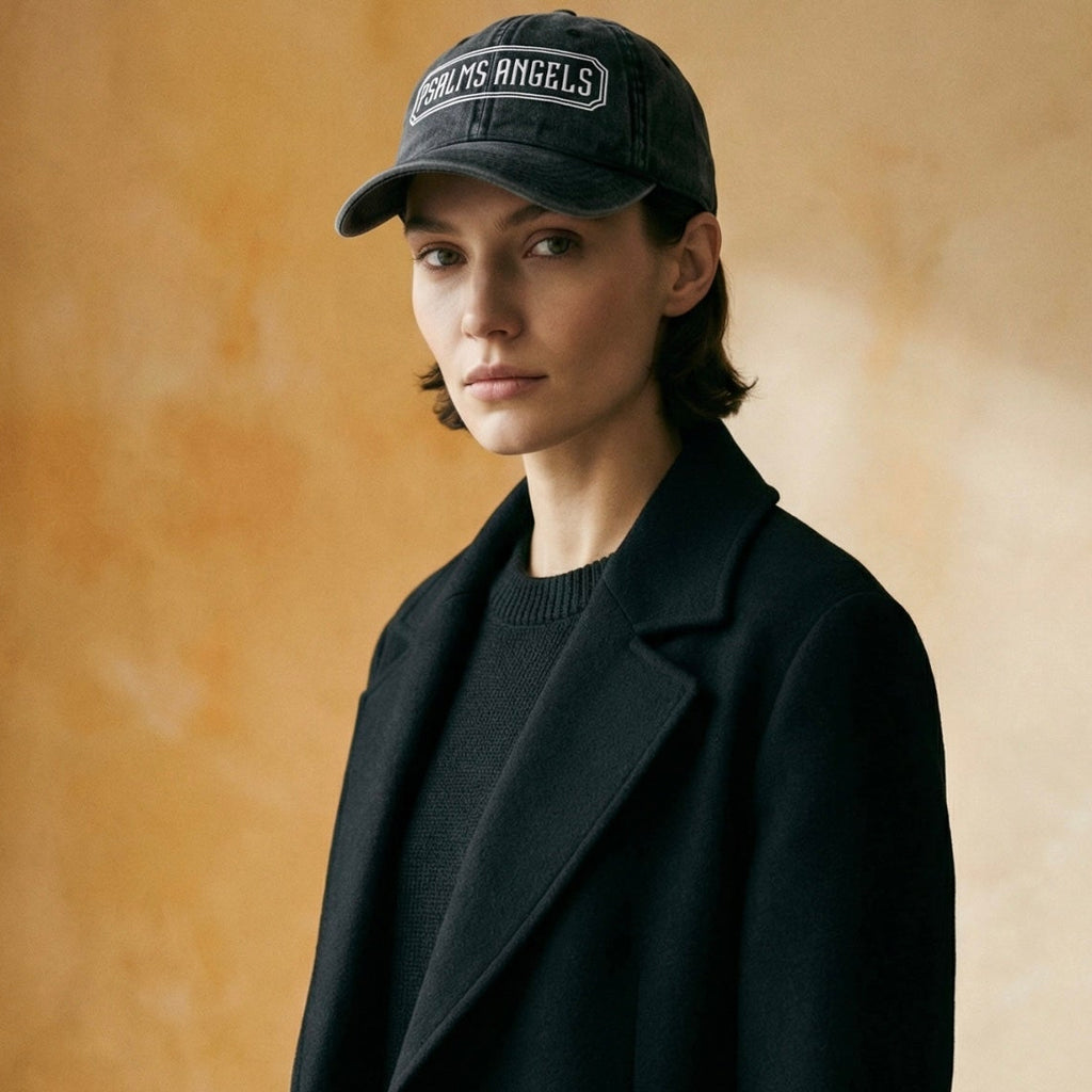Person wearing a black coat and Psalms Angels cap against a beige background